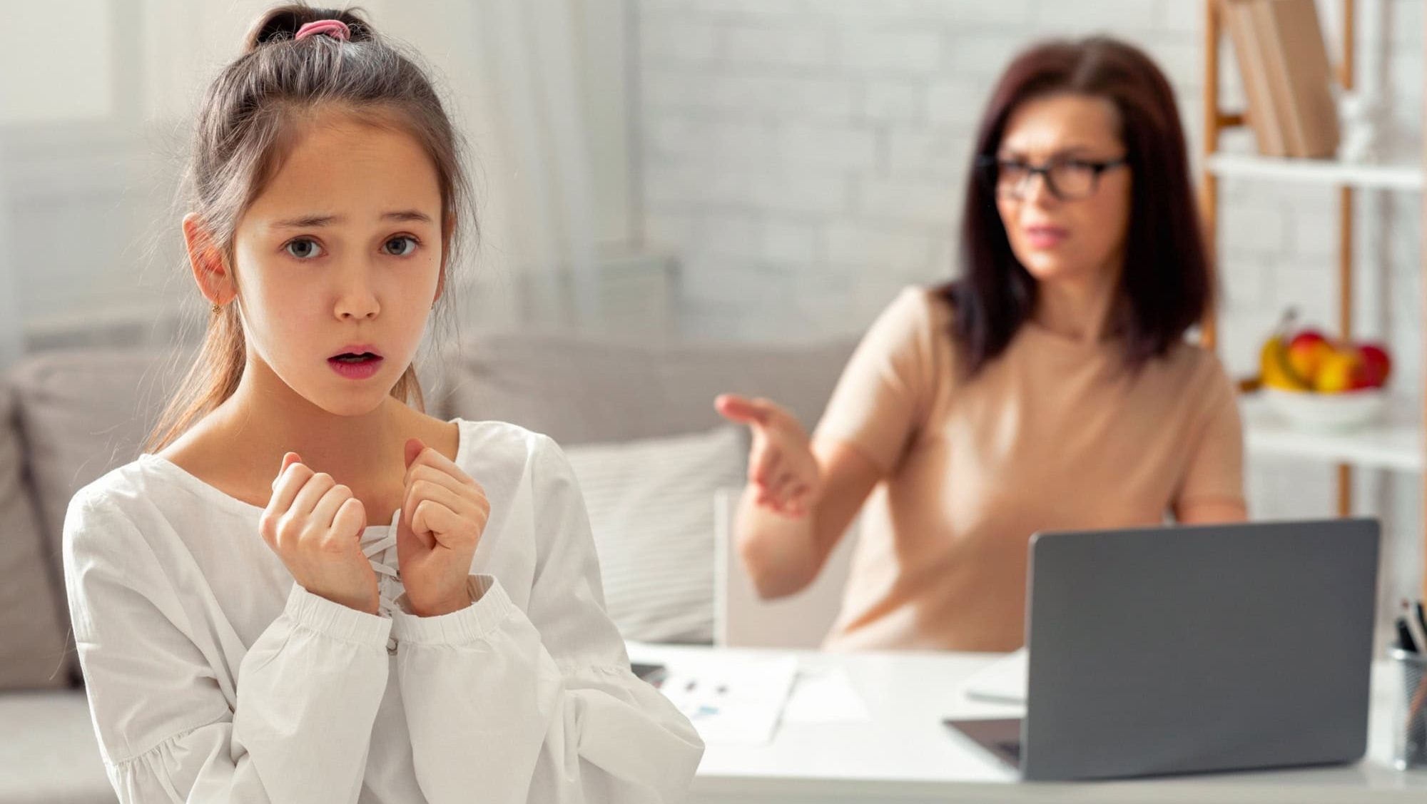 Scared teen girl feeling lonely and neglected, being scolded by her angry tired working mother at home, free space. Young woman having online job during covid-19 lockdown, having no time for her kid