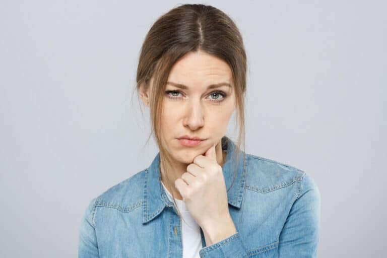 Indoor photo of attractive European lady isolated on gray background with puzzled facial expression, looking confused, tired, stressed, sad and worried, lost in problems she is facing in life.