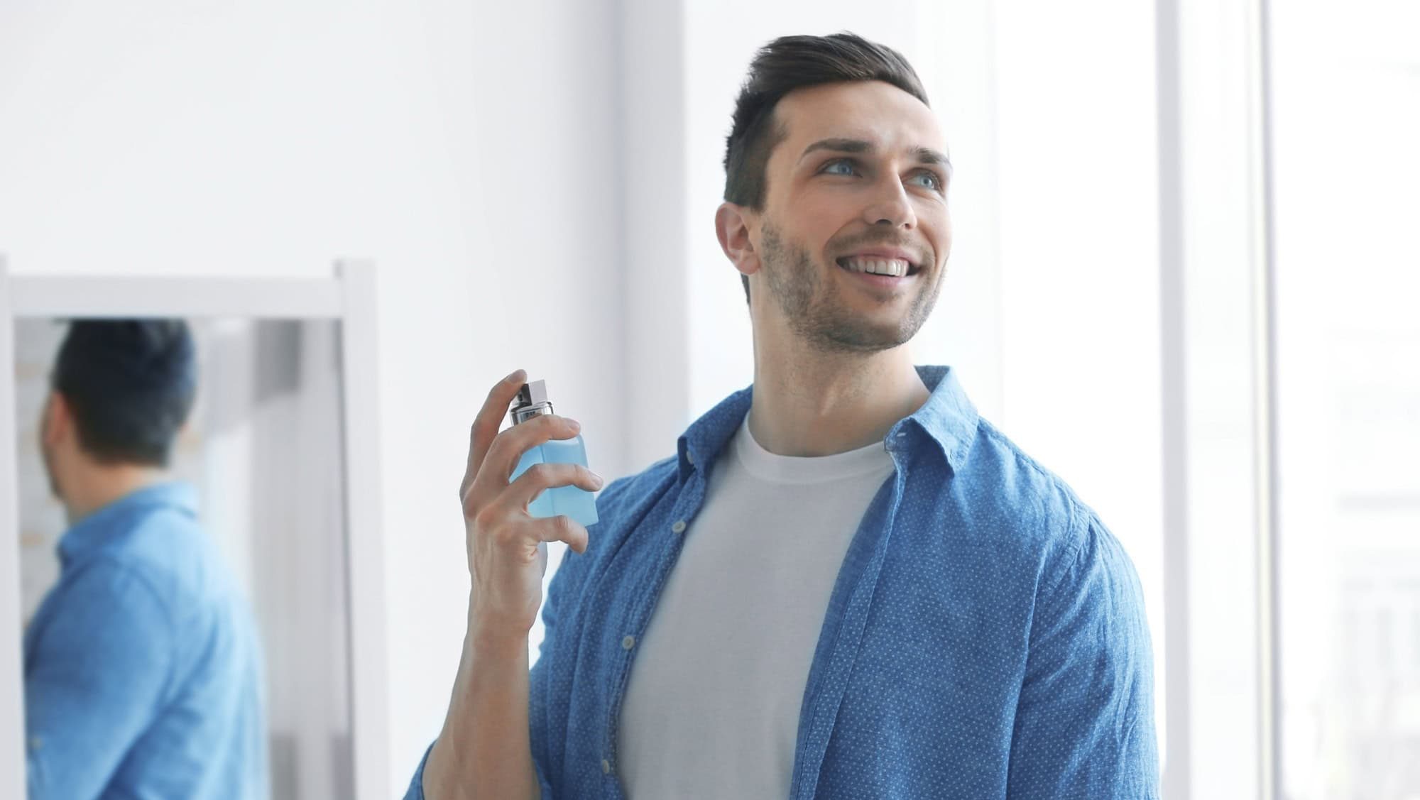 Handsome man using perfume at home