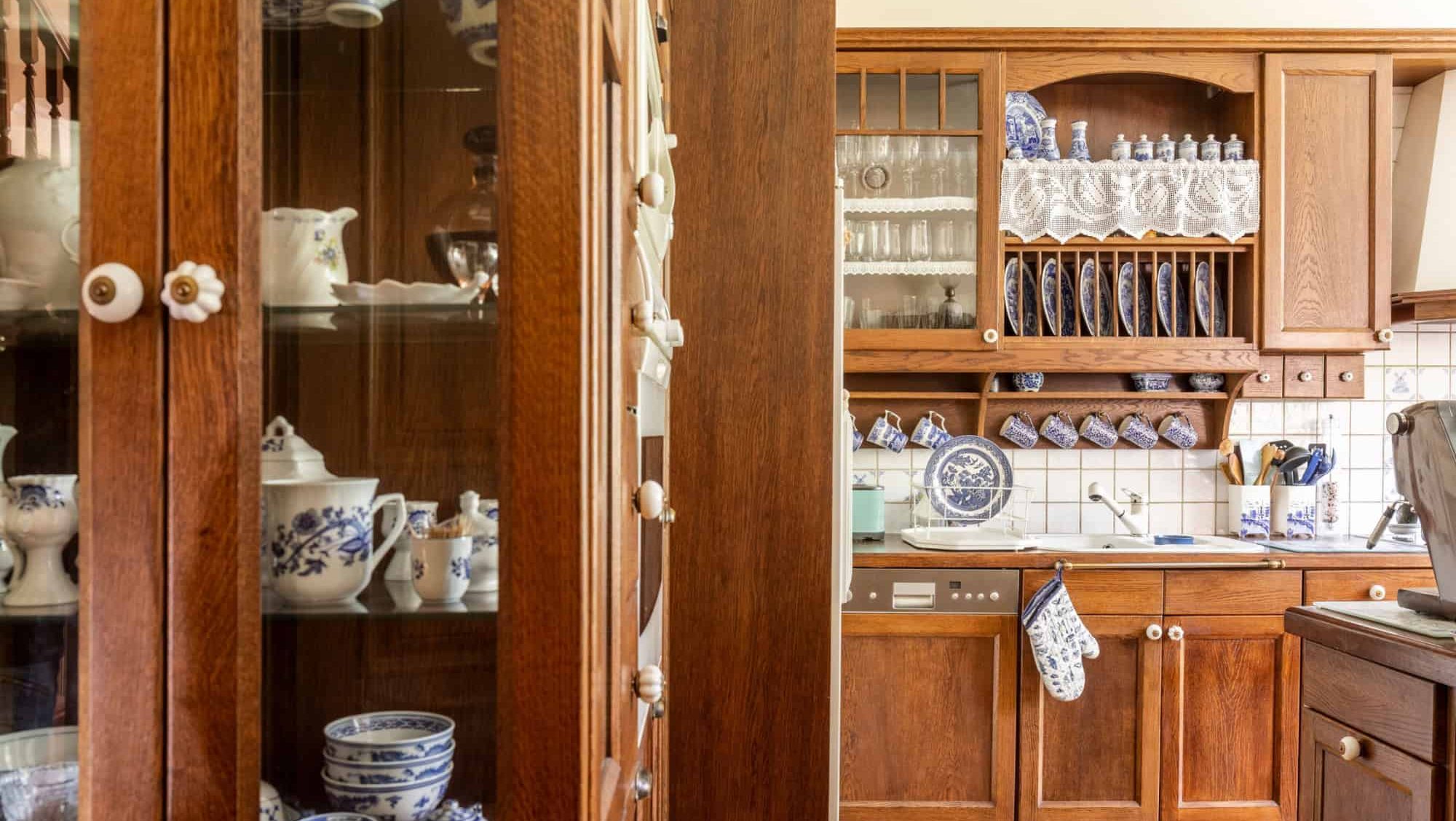Old fashioned wooden cabinets with white and cobalt blue china in kitchen interior.