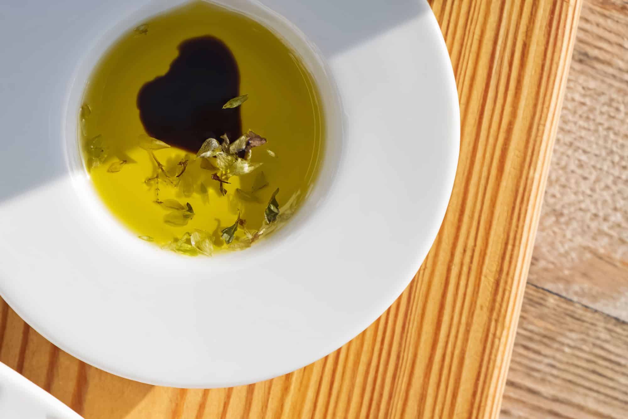 Small bowl of olive oil and balsamic vinegar, with fresh herbs for dipping bread.