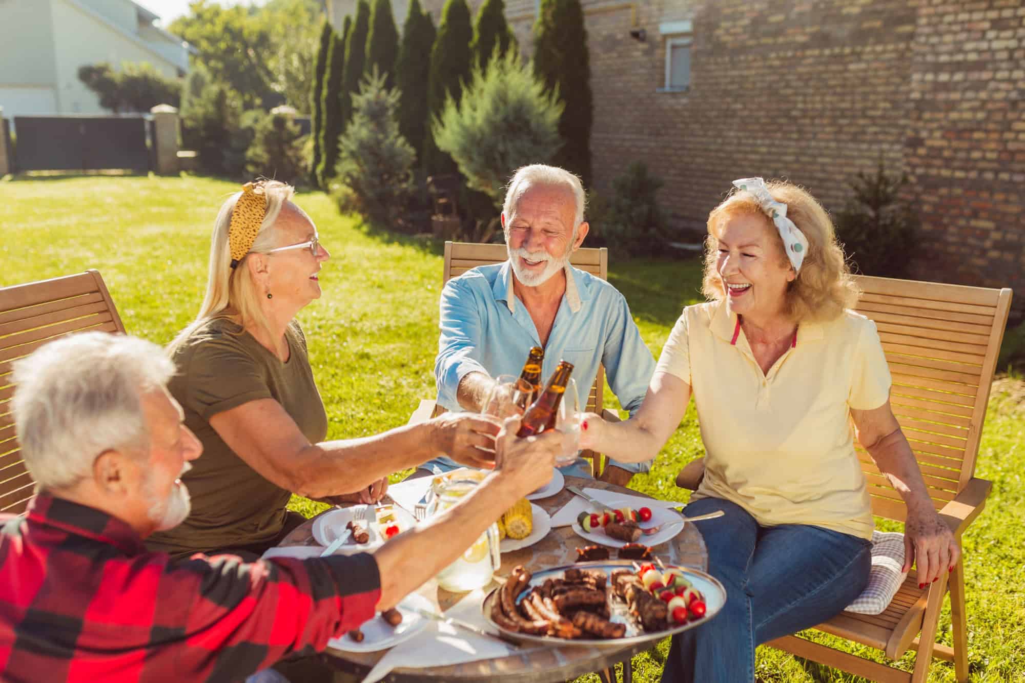 Group of senior neighbors making a toast while having an outdoor lunch in the backyard, gathered around the table, having fun spending time together