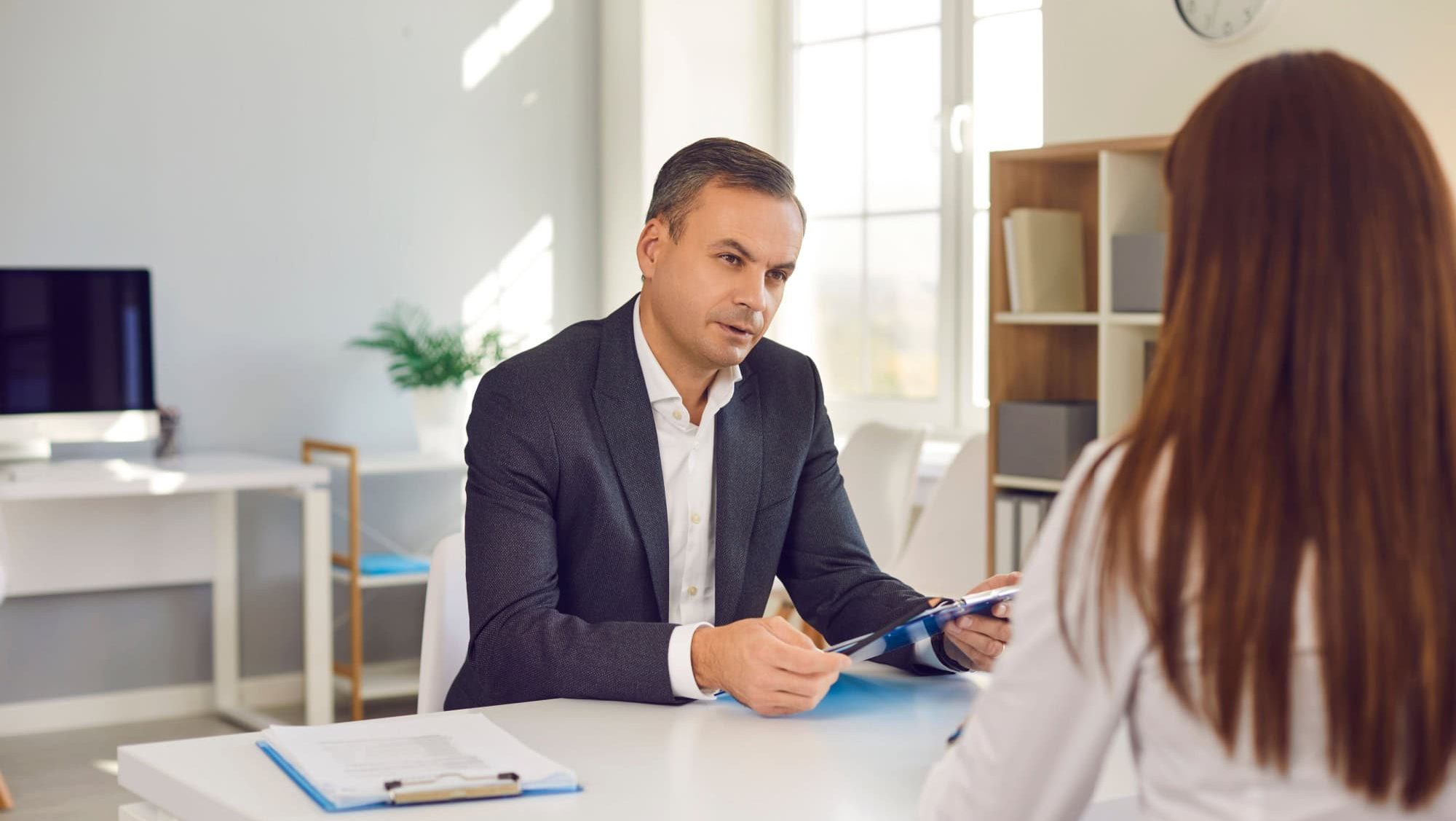 Serious male HR manager interviewing female job candidate asking her questions concerning the experience she stated on her resume. Strict employer talking to employee sitting at desk in the office