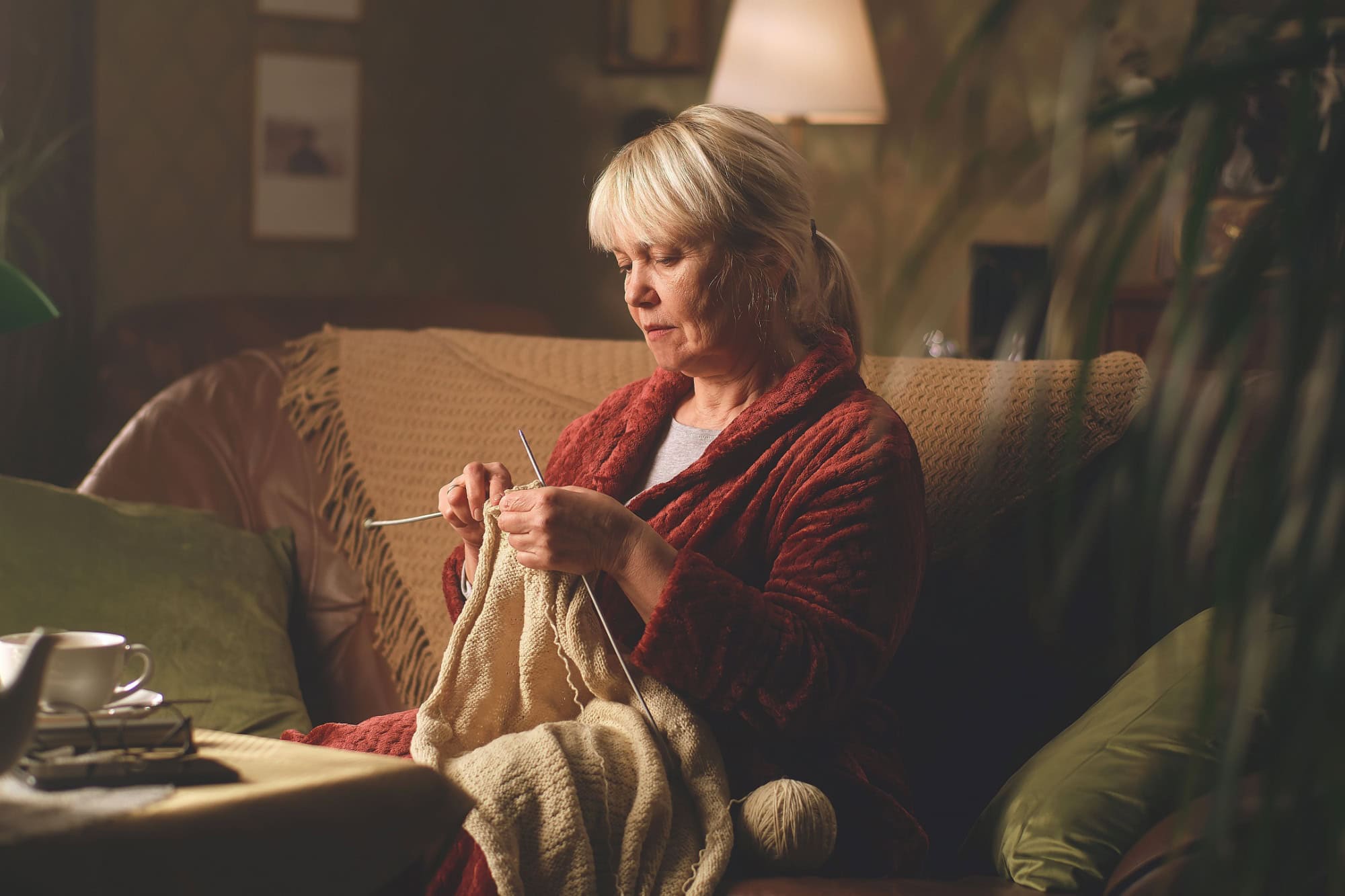 A retired woman knitting a warm sweater at night