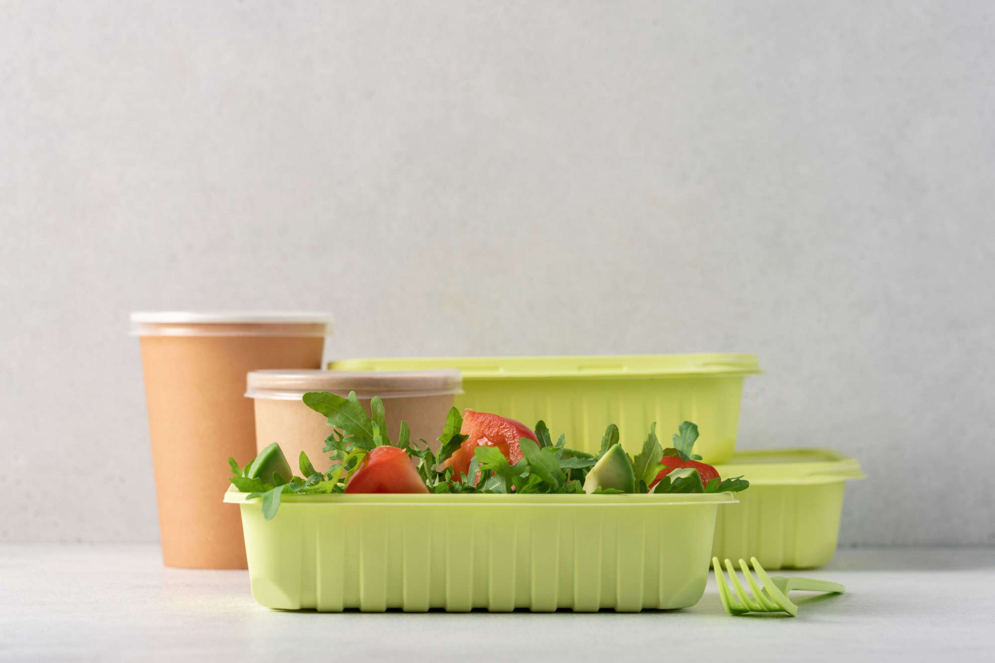 Avocado salad with tomatoes and arugula in recyclable food container. Eco food delivery concept