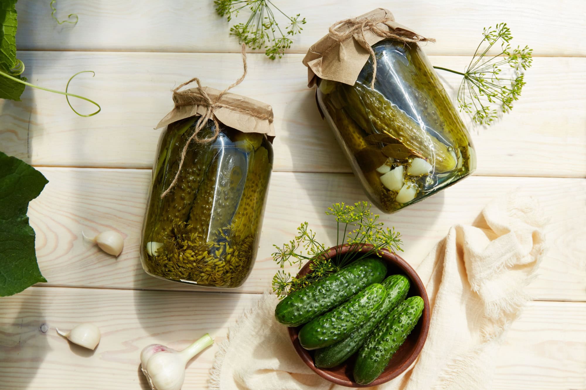 Pickled cucumbers in jars, fresh cucumbers on bowl, dill, garlic on a white wooden background. Home canning. Top view.