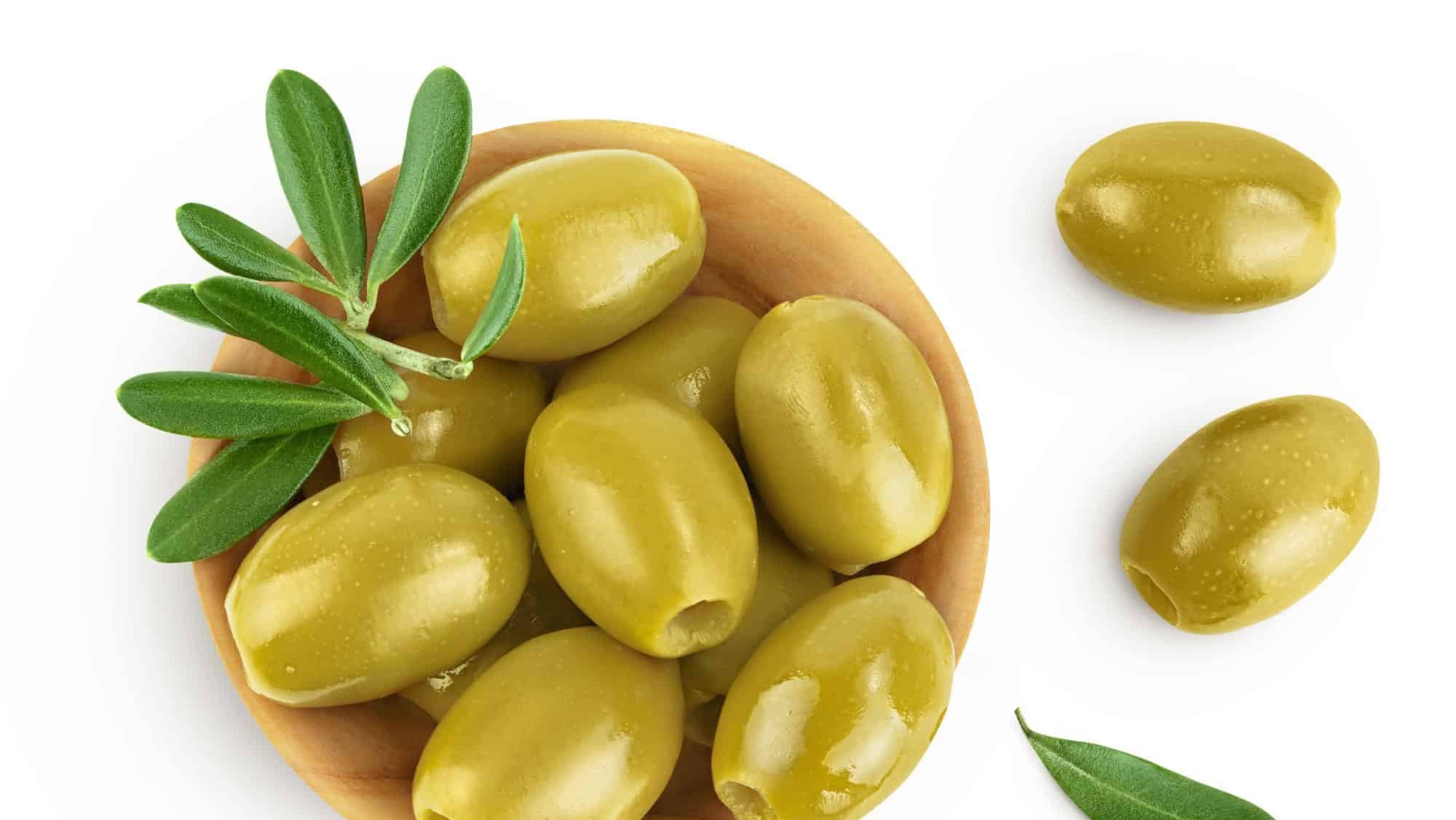 Green olives with leaves in wooden bowl isolated on a white background with full depth of field. Top view. Flat lay