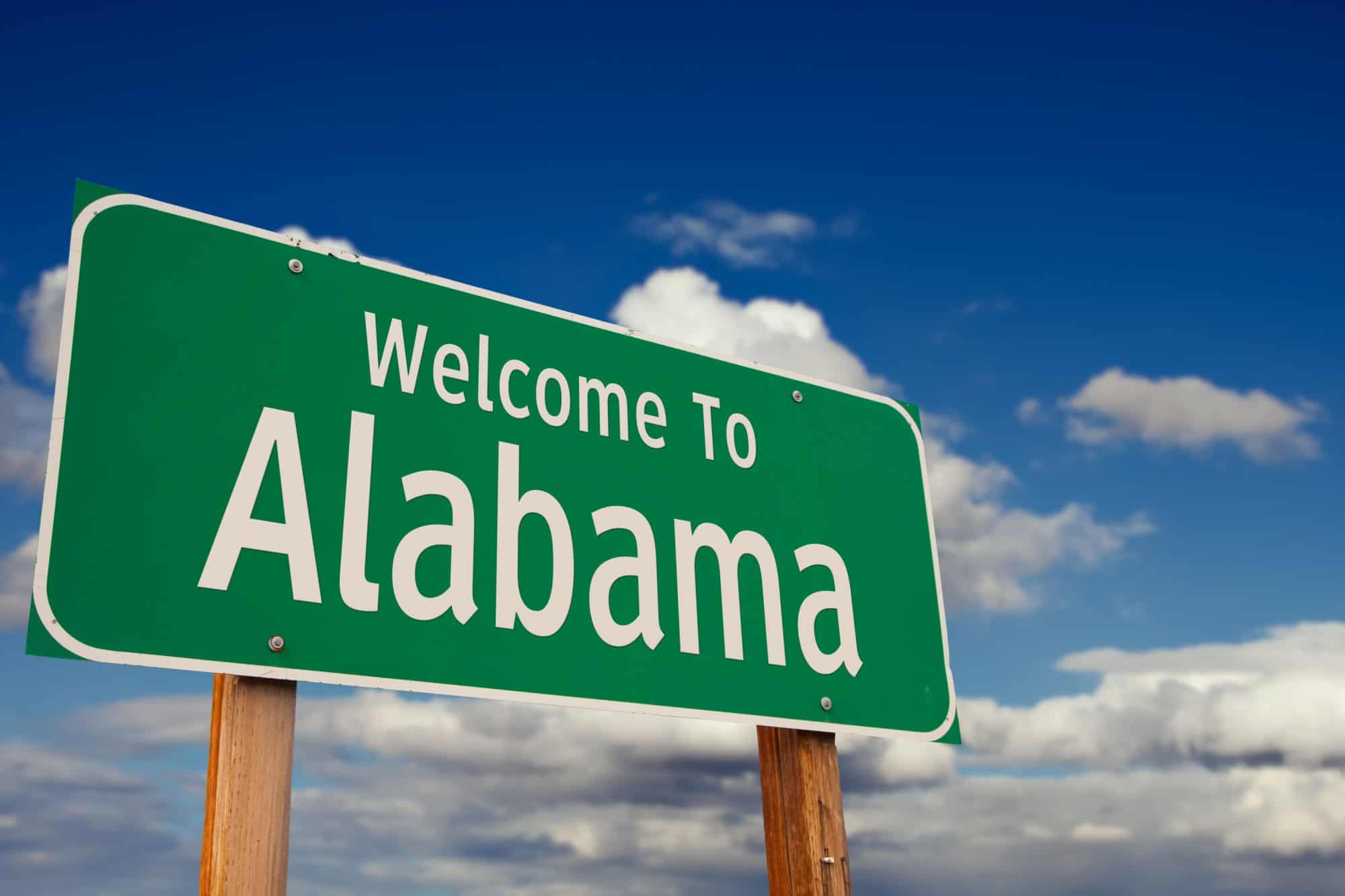 Welcome To Alabama Green Road Sign Over Blue Sky with Some Clouds.