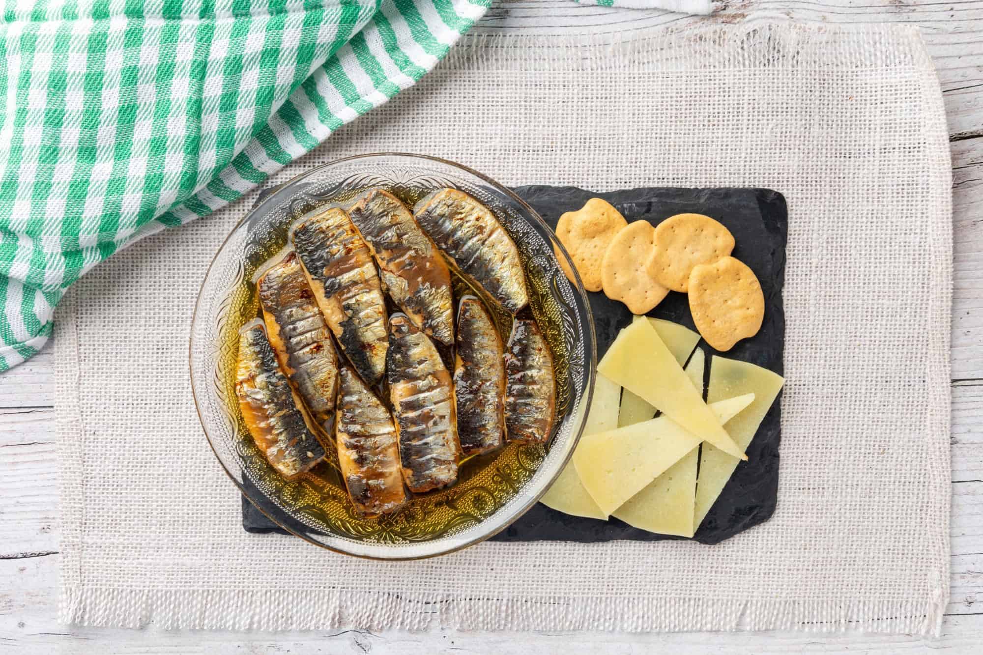 Sardines arranged in an ornate glass bowl filled with oil, displayed on a light-colored woven placemat, capturing rustic culinary elegance.