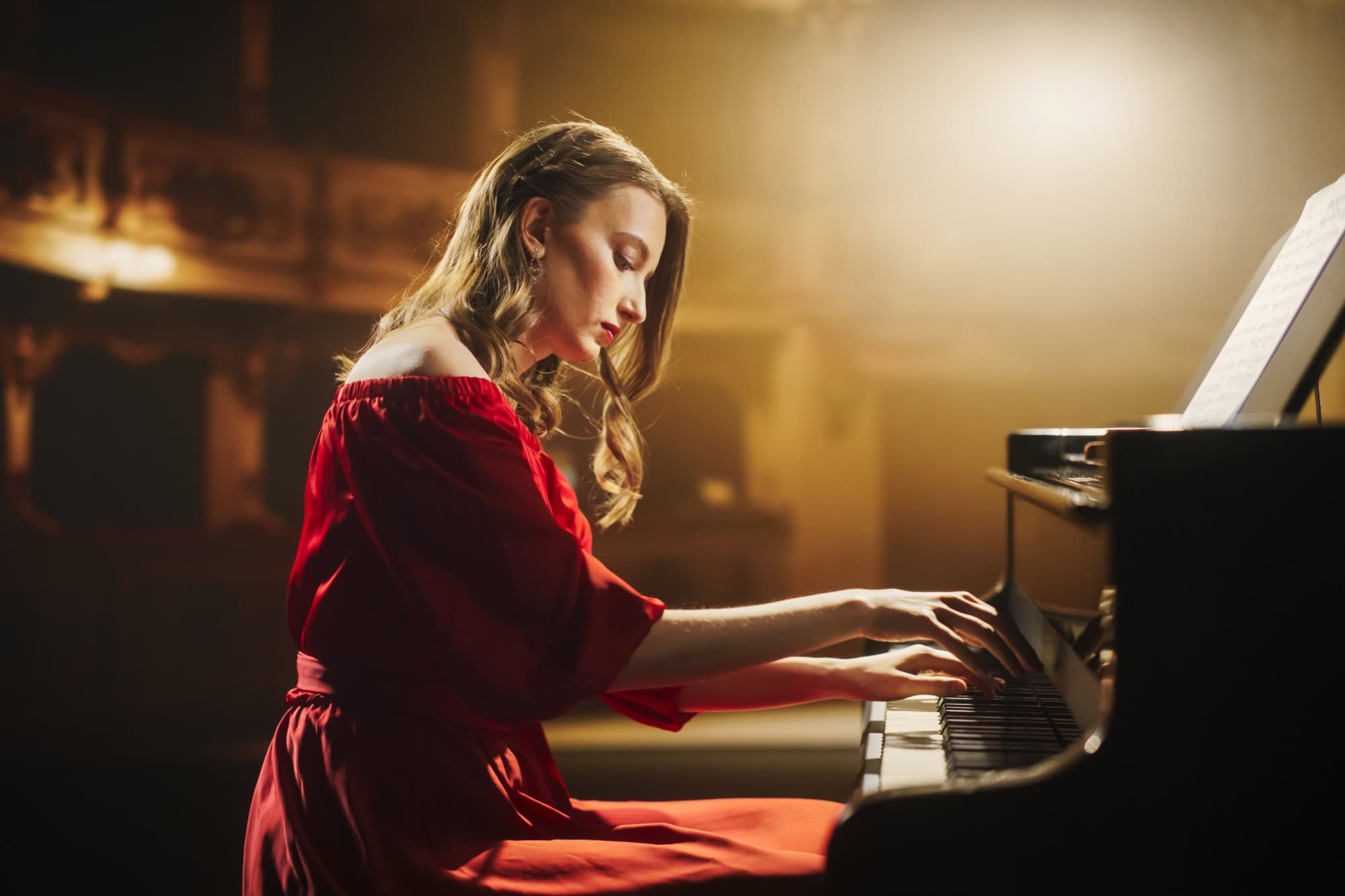 Classical Piano Concert: Under the Spotlight, Young Female Pianist in a Red Dress Delivering a Powerful Performance on the Grand Piano. Elegant Stage Setting Complements Her Passionate Playing