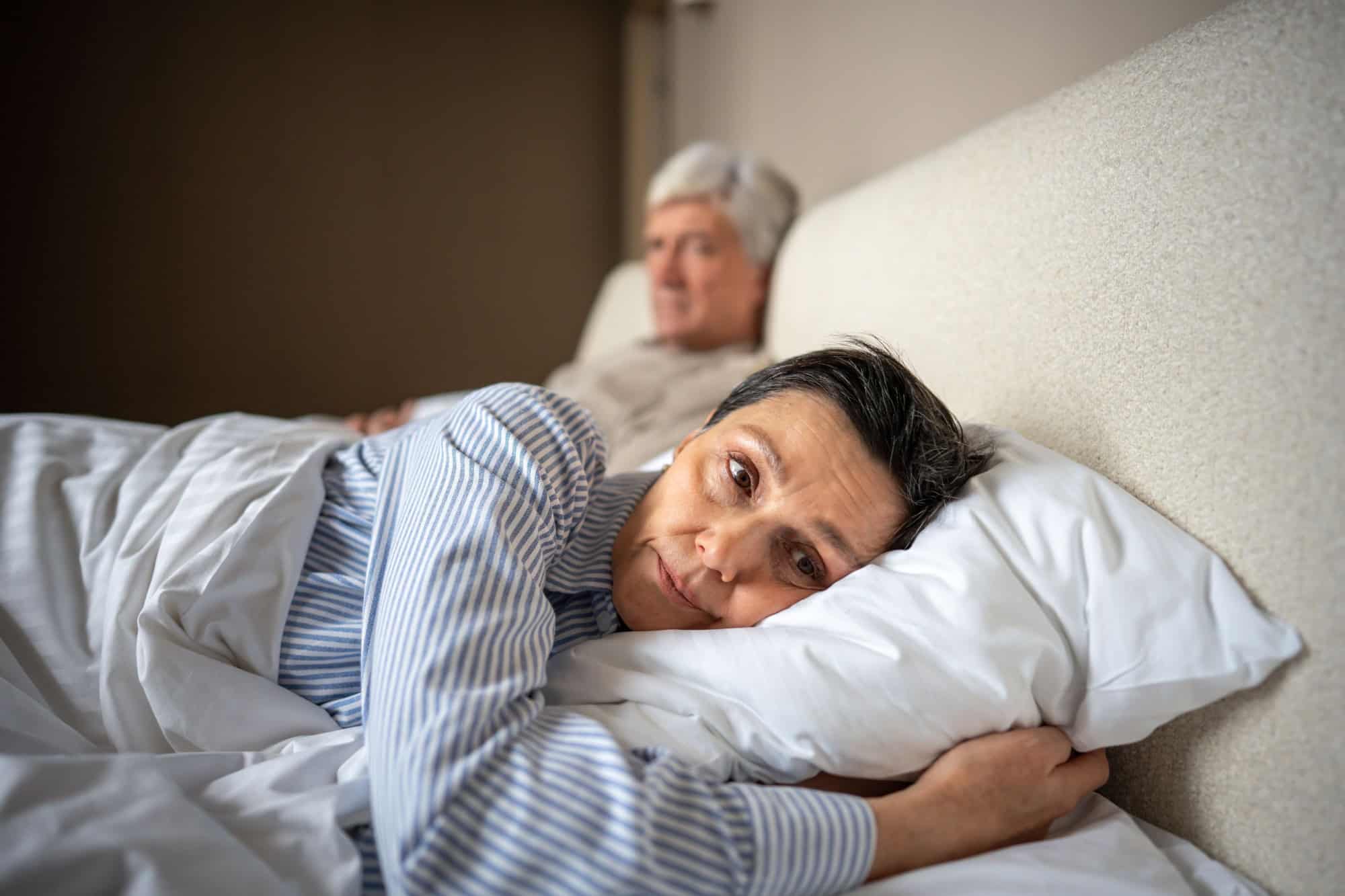 Senior couple in crisis, upset wife rejecting husband after quarrel, thinking about marriage, lying in bed together. Lost intimacy trust, spouse couple strain, emotional disconnect, cheating.