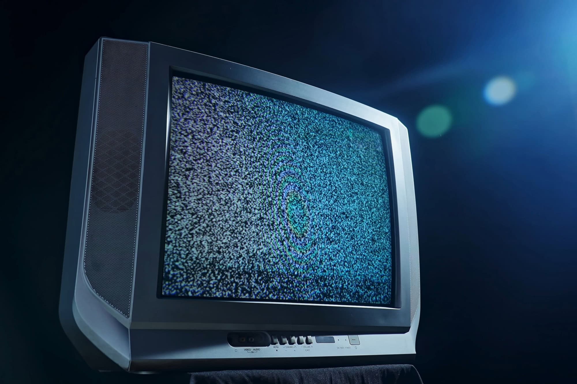 A vintage CRT television set emits static noise in a dimly lit room, highlighting nostalgic technology contrasts.