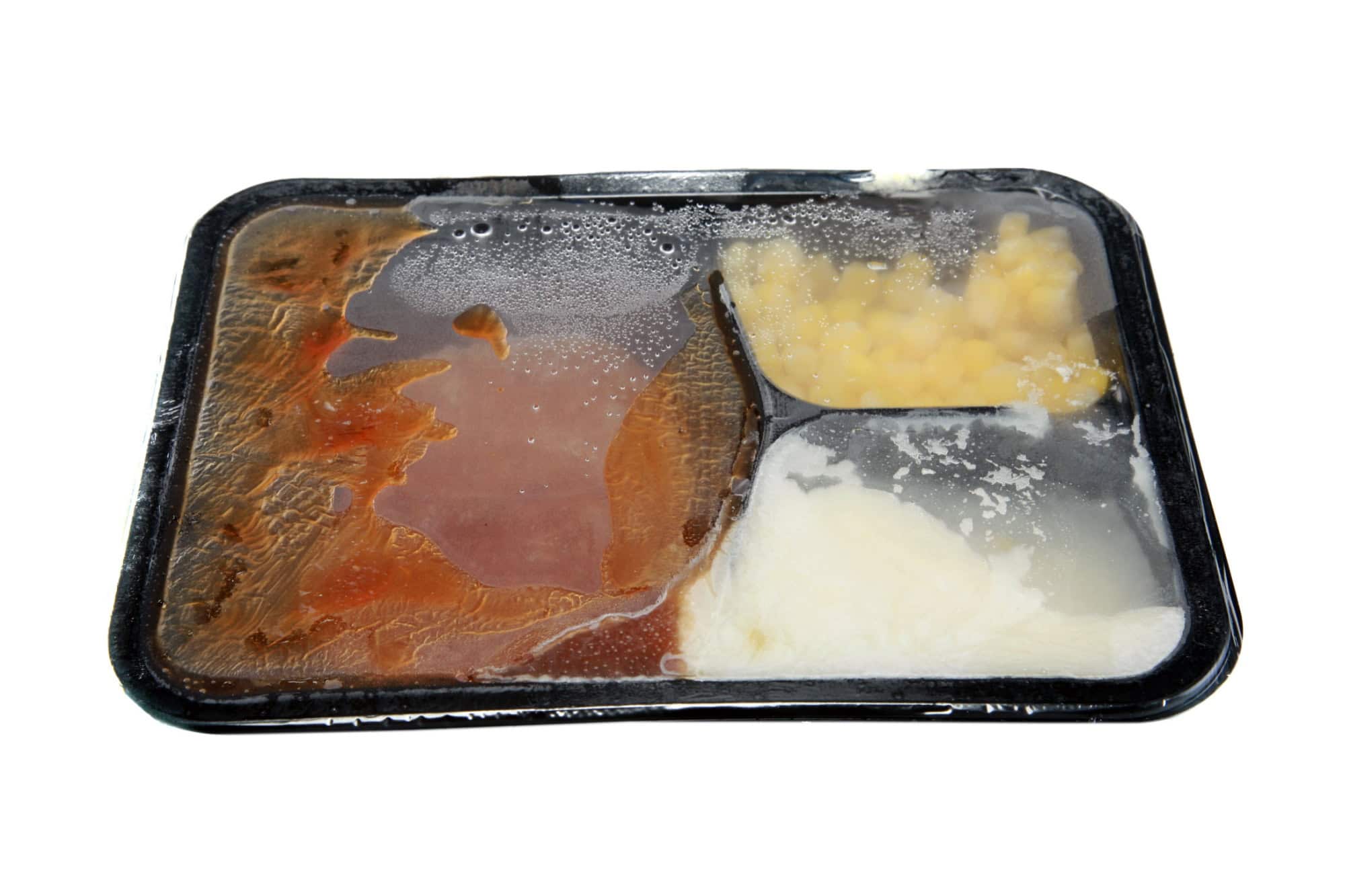 a classic salisbury steak tv dinner with mashed potatoes and corn in its black plastic tray, isolated on white