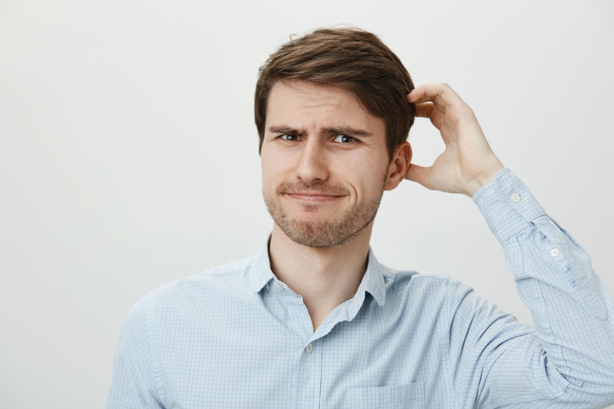 Puzzled ordinary european guy with bristle scratching head while looking with frustration at camera, being questioned or forgetting important information. Man cannot remember where he put keys