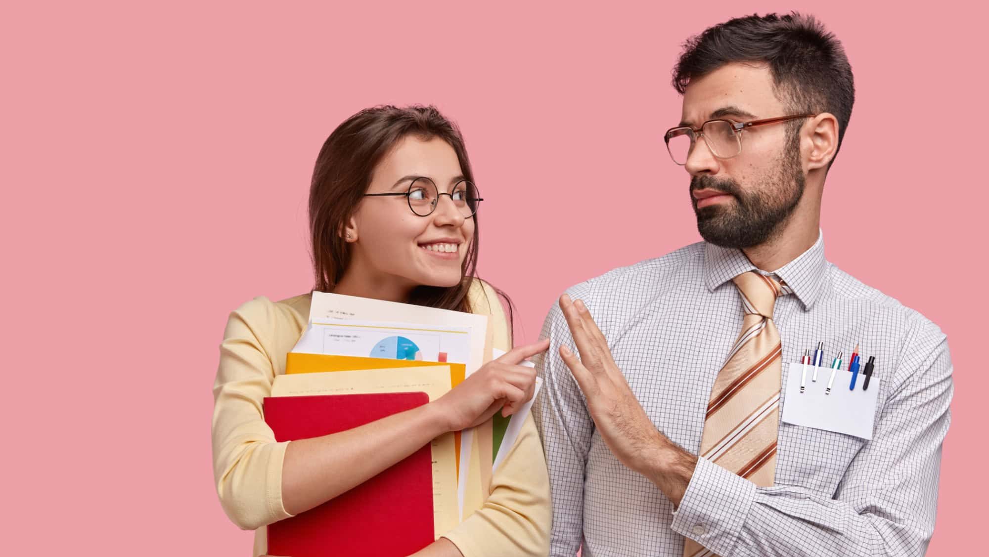 Positive schoolgirl carries papers and notepad, asks friend for help, has glad expression, wears spectacles, isolated over pink background. Bearded young man demonstrates refusal gesture to girlfriend
