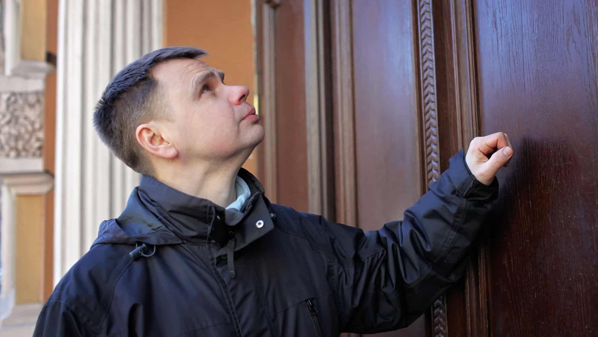 Middle-aged man waiting in front of wooden house door and thinking to knock or not to knock, people relationship, date and meeting concept, outdoor