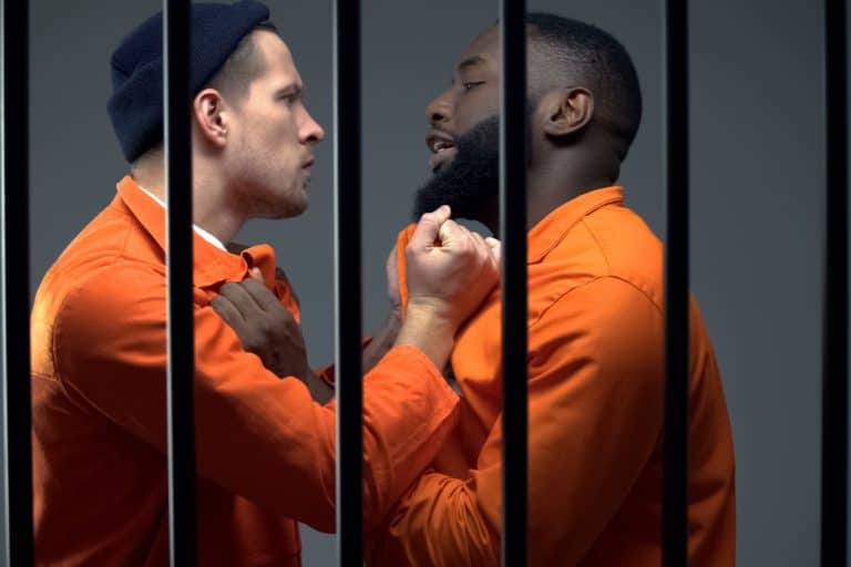 Black and caucasian prisoners having fight in cell, jail overcrowding, conflict