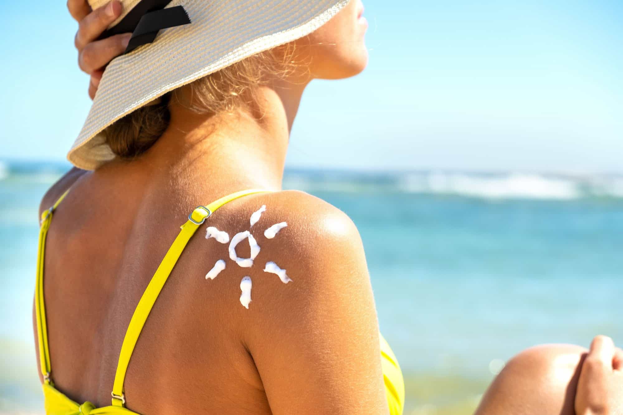 Back view of young woman tanning at the beach with sunscreen cream in sun shape on her shoulder. UV sunburn protection and sunblock skincare concept