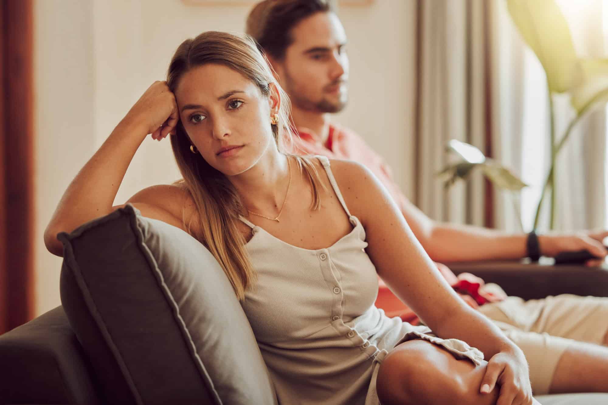 Unhappy, sad and annoyed couple after a fight and are angry at each other while sitting on a couch at home. A woman is stressed, upset and frustrated by her boyfriend after an argument