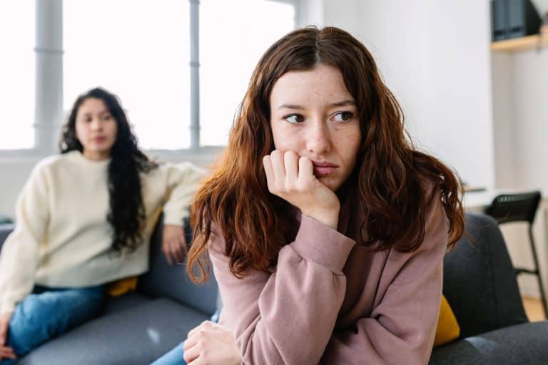 Two angry female friends sitting separately on sofa at home after an argument