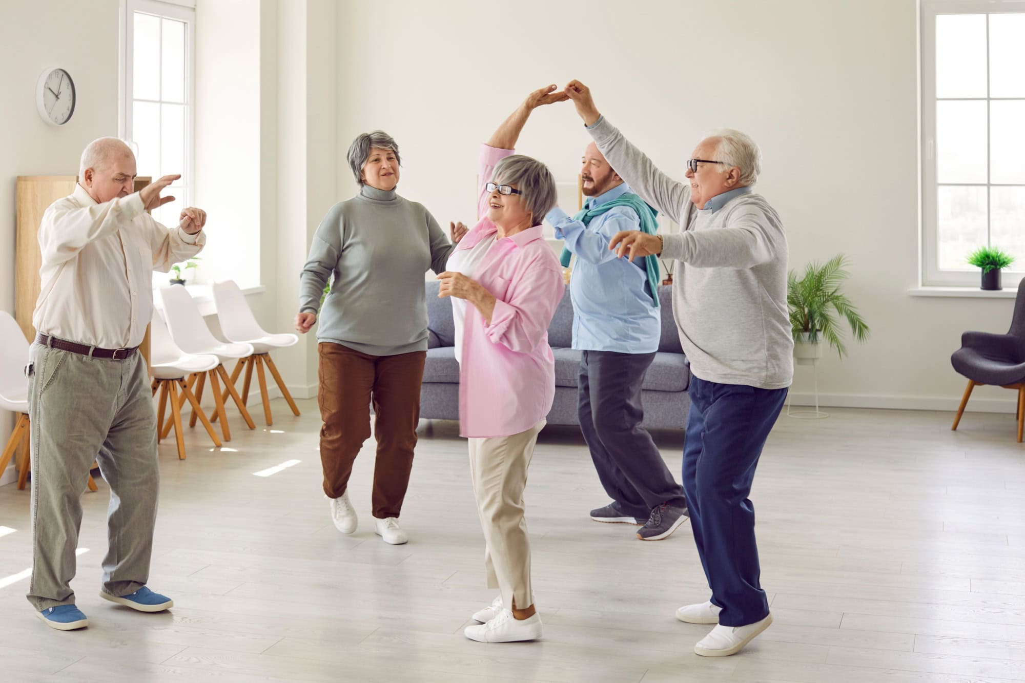 Retirement community. Elderly men and women actively spend time having fun and dancing at party in nursing home. Group of senior Caucasian people laughing and dancing together in living room.