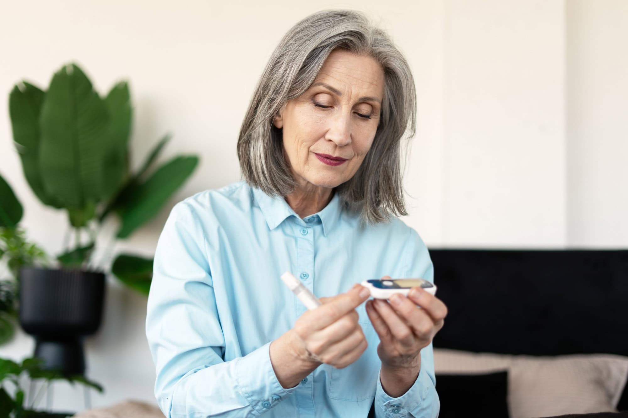 Elderly woman checking blood sugar levels at home, using a lancet and glucometer for diabetes management in her cozy living room