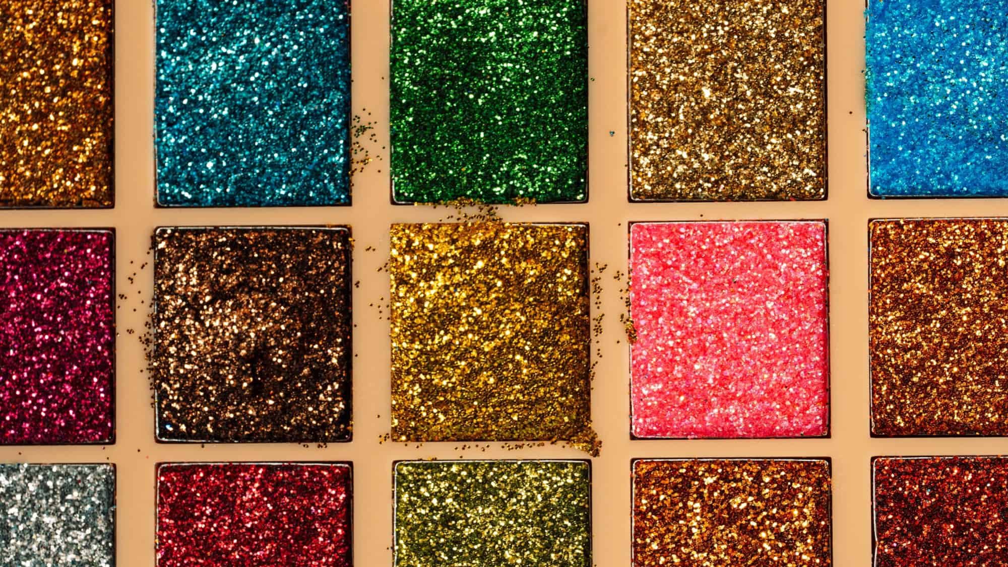 Close-up of colorful glitter eyeshadows in used palette. Textured beauty concept with bold sparkle.