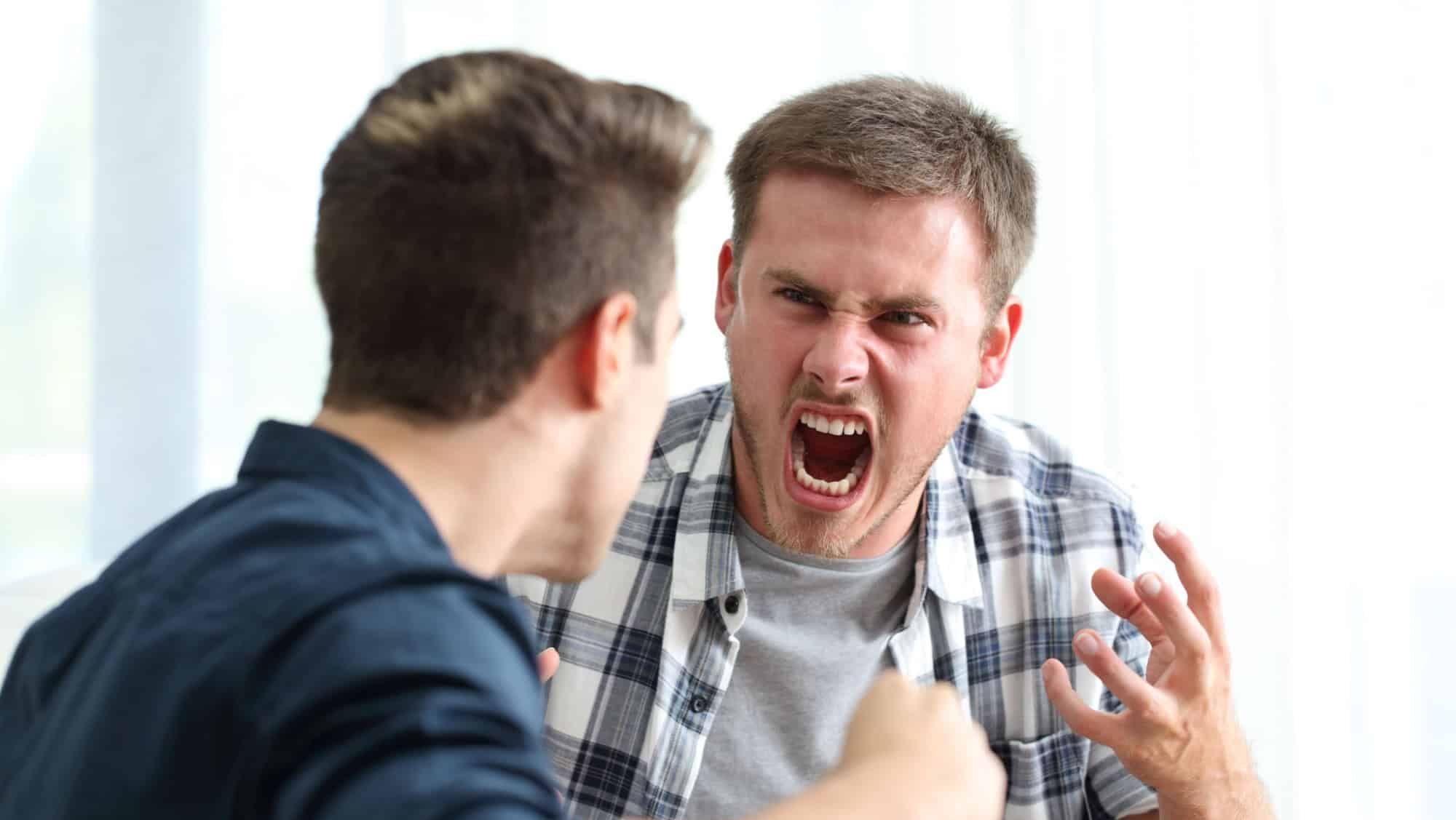 Two angry friends or roommates arguing and threatening in the living room at home