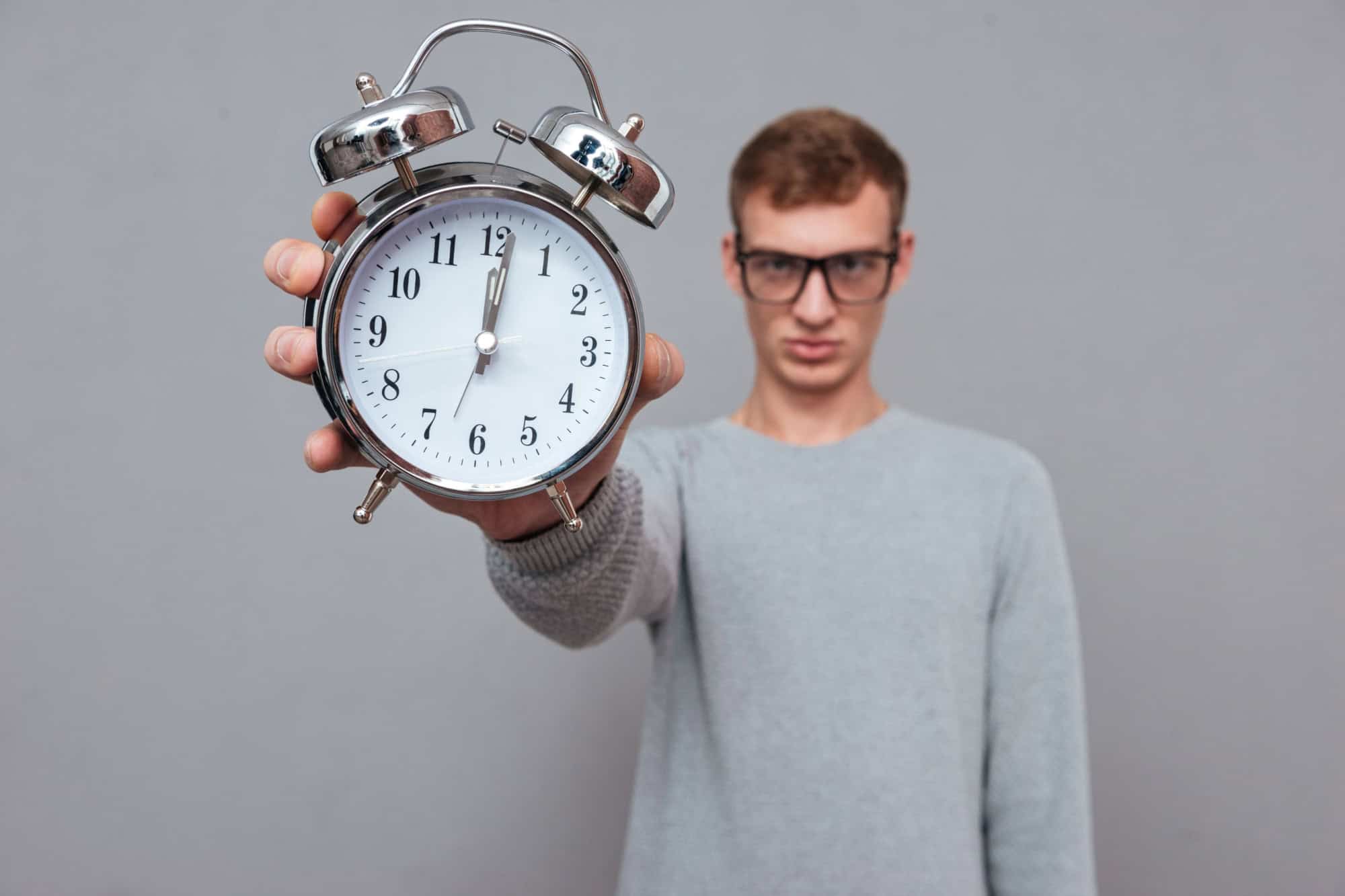 Man in glasses showing clock ant camera. in studio. isolated gray background? Focus on clock