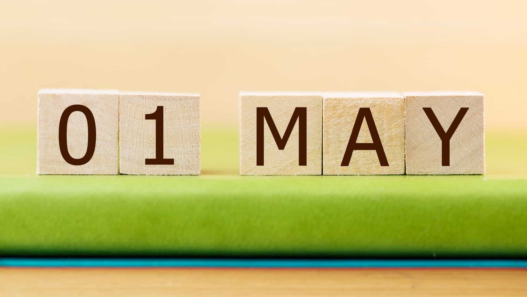 Wooden cube shape calendar for MAY 1 on green book, table.