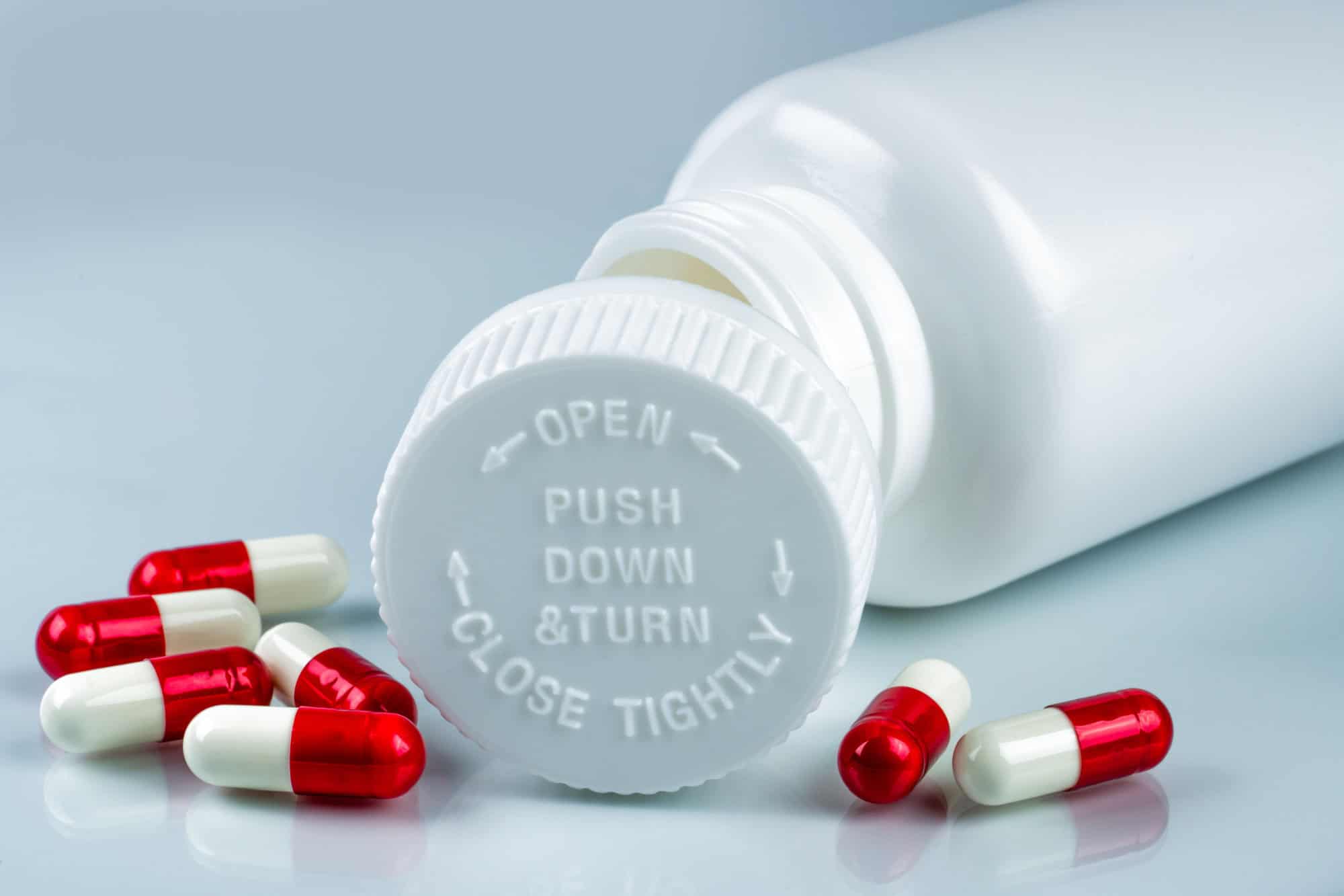Capsules pills on white background and plastic bottle with blank label and copy space. Childproof packaging. Child resistant pill container. Push down and turn cap.Global healthcare and love concept.