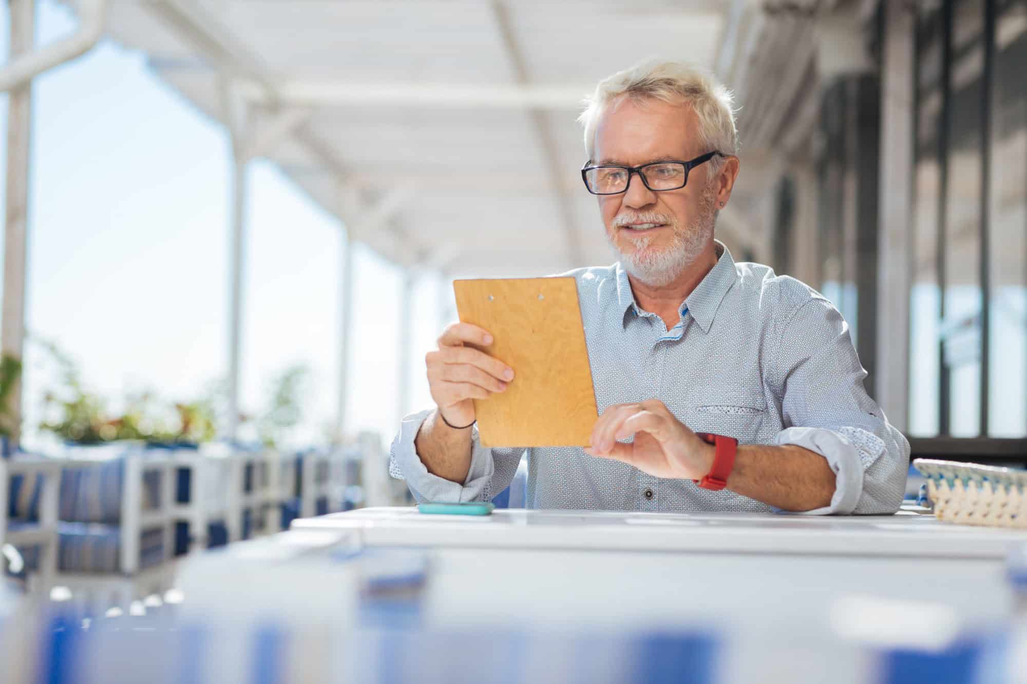 What to choose. Positive nice elderly man reading the menu while sitting in the restaurant