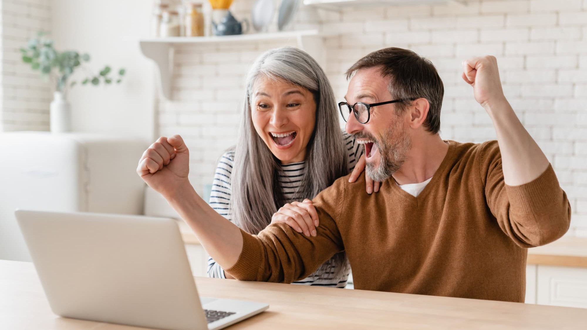 Happy excited mature middle-aged couple celebrating success in business, paying bills, lottery win, investment, startup, pension, refunds, payment at home using laptop