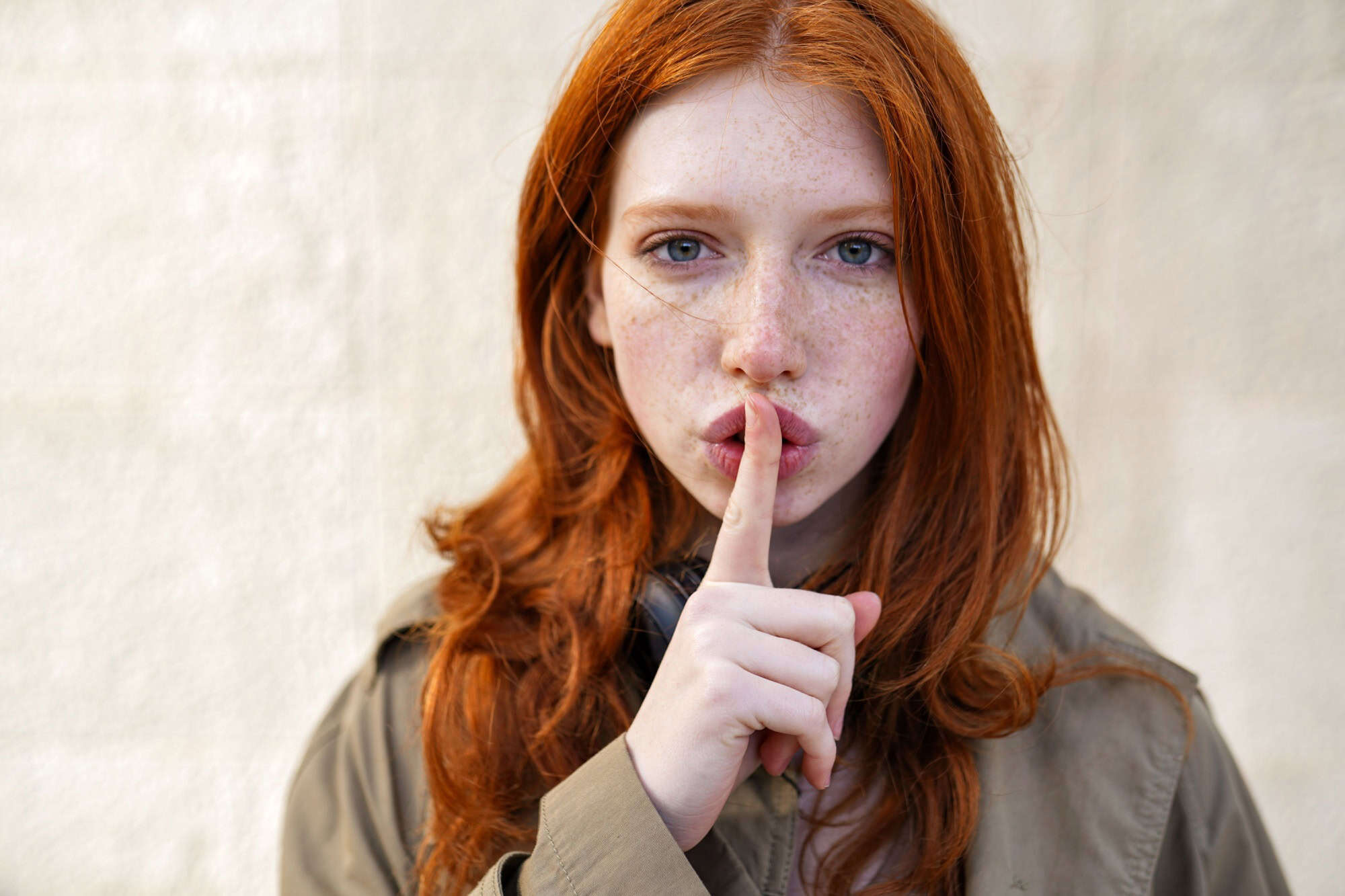 Hipster teen gen z redhead girl showing shh sign finger gesture asking to keep secret, be hush silent or privacy silence on urban wall background. Teenage problem secrecy concept. Close up portrait