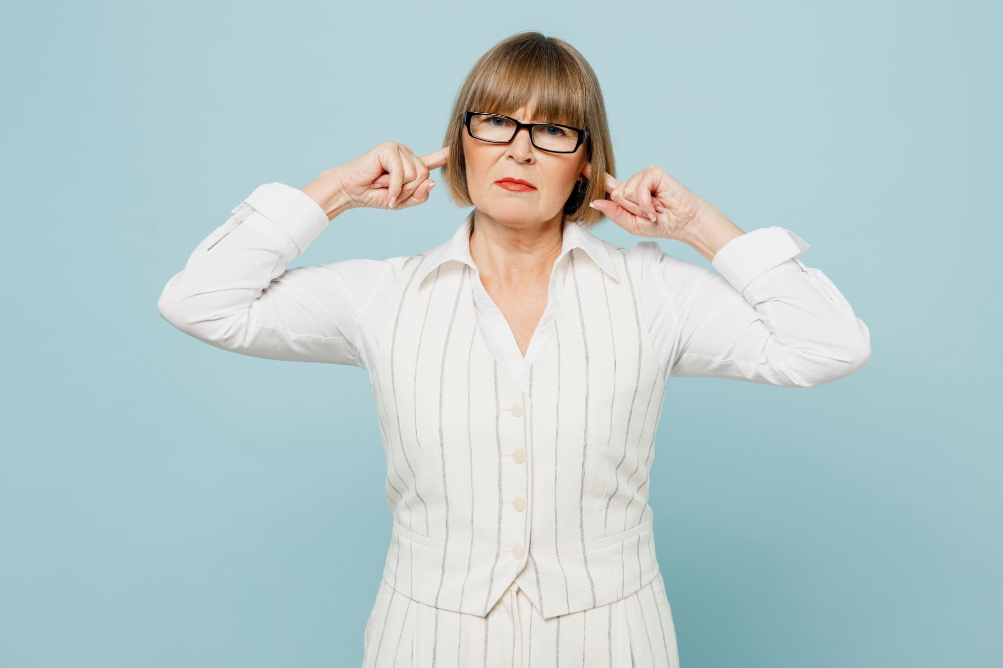 Sad employee business woman 50s wear white classic suit glasses formal clothes cover ears with hands fingers do not want to listen scream isolated on plain blue background. Achievement career concept