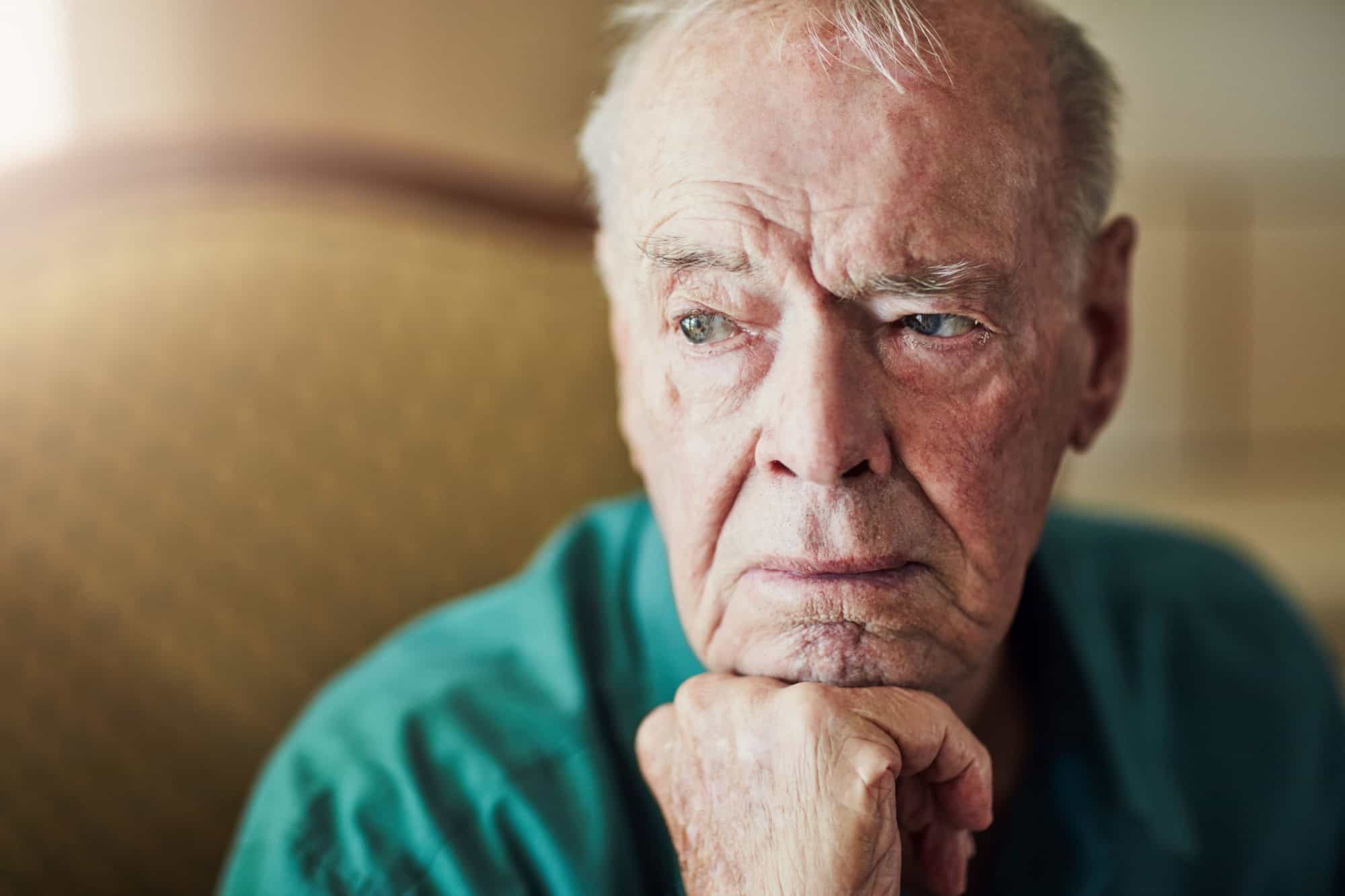 Elderly, man and sad with thinking of memory in retirement home with remember, nostalgia or reflection on sofa. Senior, person and lonely with alzheimers, depression and thoughtful on couch in lounge