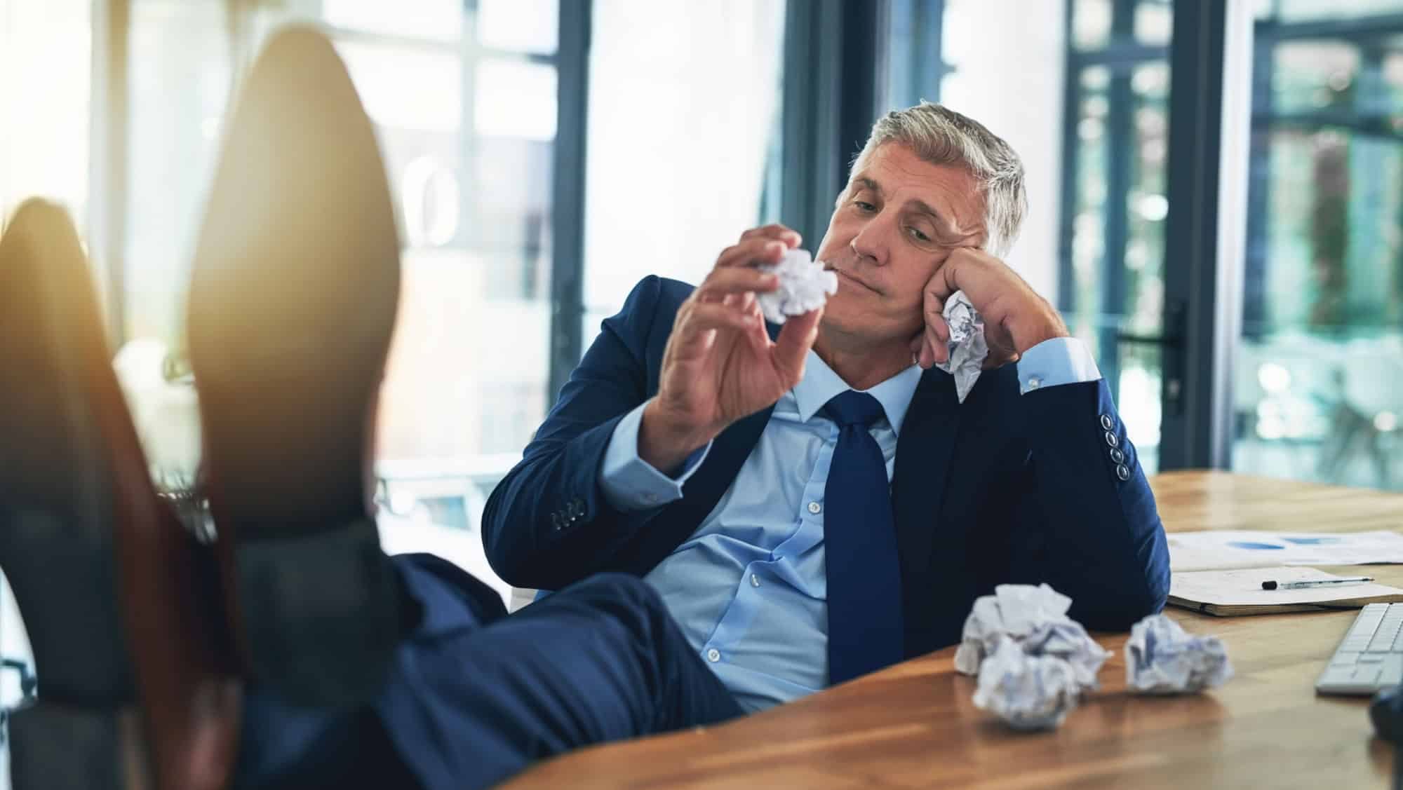 Bored, businessman and crumpling paper in office for procrastination, distraction and relax with deadline pressure. Lazy, male person and paperwork crisis, burnout and lack of motivation for work
