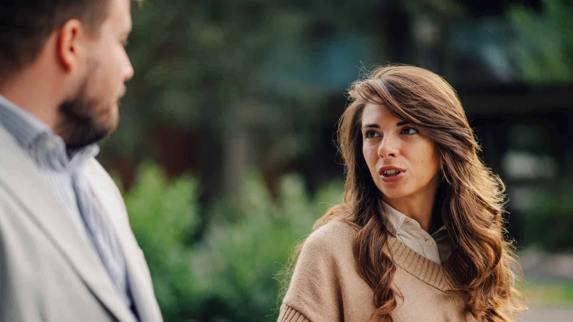 Young professional woman is gesturing with her hand while explaining herself during a difficult conversation with a man outdoors