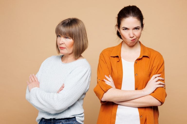 Elder sad mad parent mom 50s years old with young adult daughter two women together wear casual clothes hold hands crossed folded isolated on plain pastel light beige background. Family day concept
