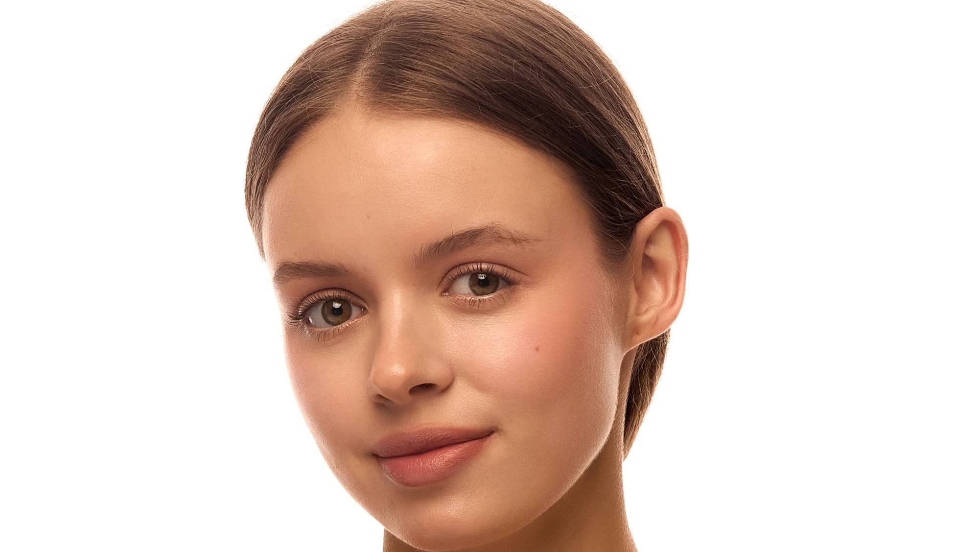 Portrait of beautiful woman with clean natural makeup, flawless skin, smooth hair tied back and subtle smile under white background. Concept of beauty, skin glow, youth, cosmetic product