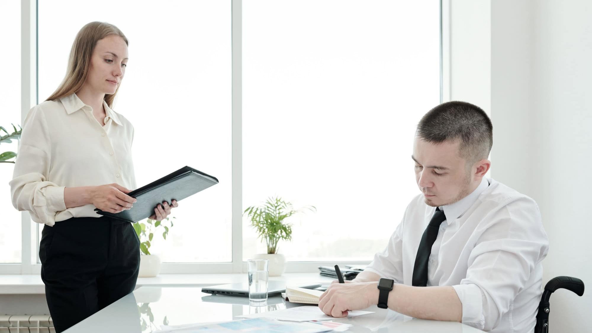 Young secretary looking at boss signing document by table