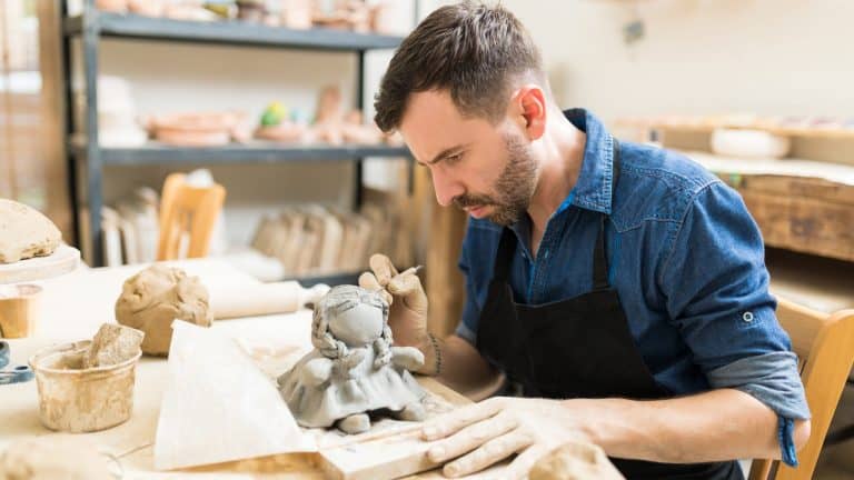 Confident male owner making clay sculpture of doll at workbench in workshop