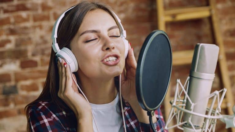 Woman in headphones recording music video blog home lesson, singing or making broadcast internet tutorial while sitting in loft workplace or at home. Concept of hobby, music, art and creation.