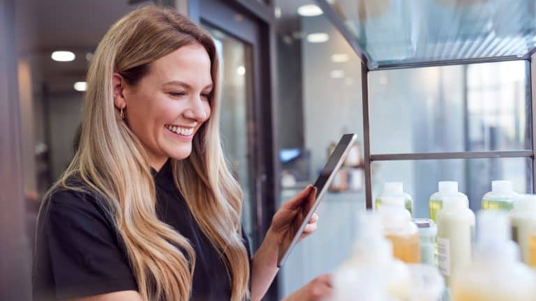 Female Stylist Or Business Owner In Hairdressing Salon Using Digital Tablet To Check Beauty Products