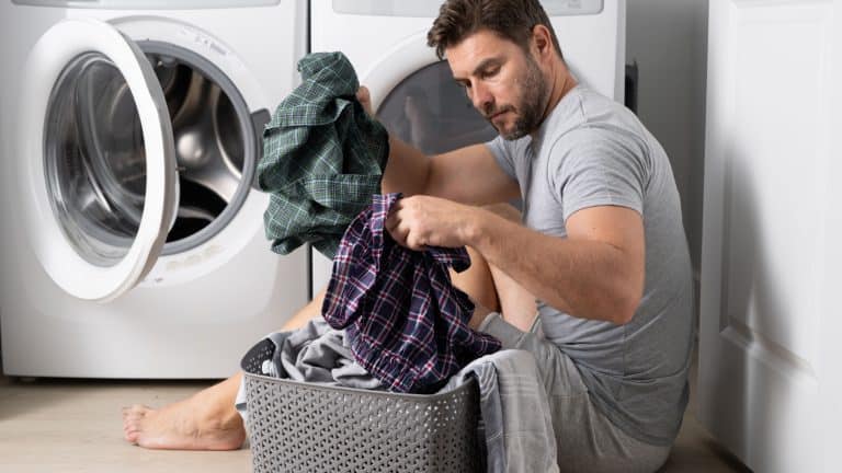 Man with clothes near washing machine. Laundry cleaning. Housework, homework, male housekeeper. Husband man doing laundry at home. Washer and dryer at home.