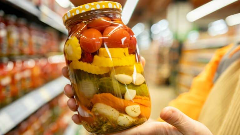 Colorful jar of pickled vegetables held by a shopper in a grocery store aisle during the daytime