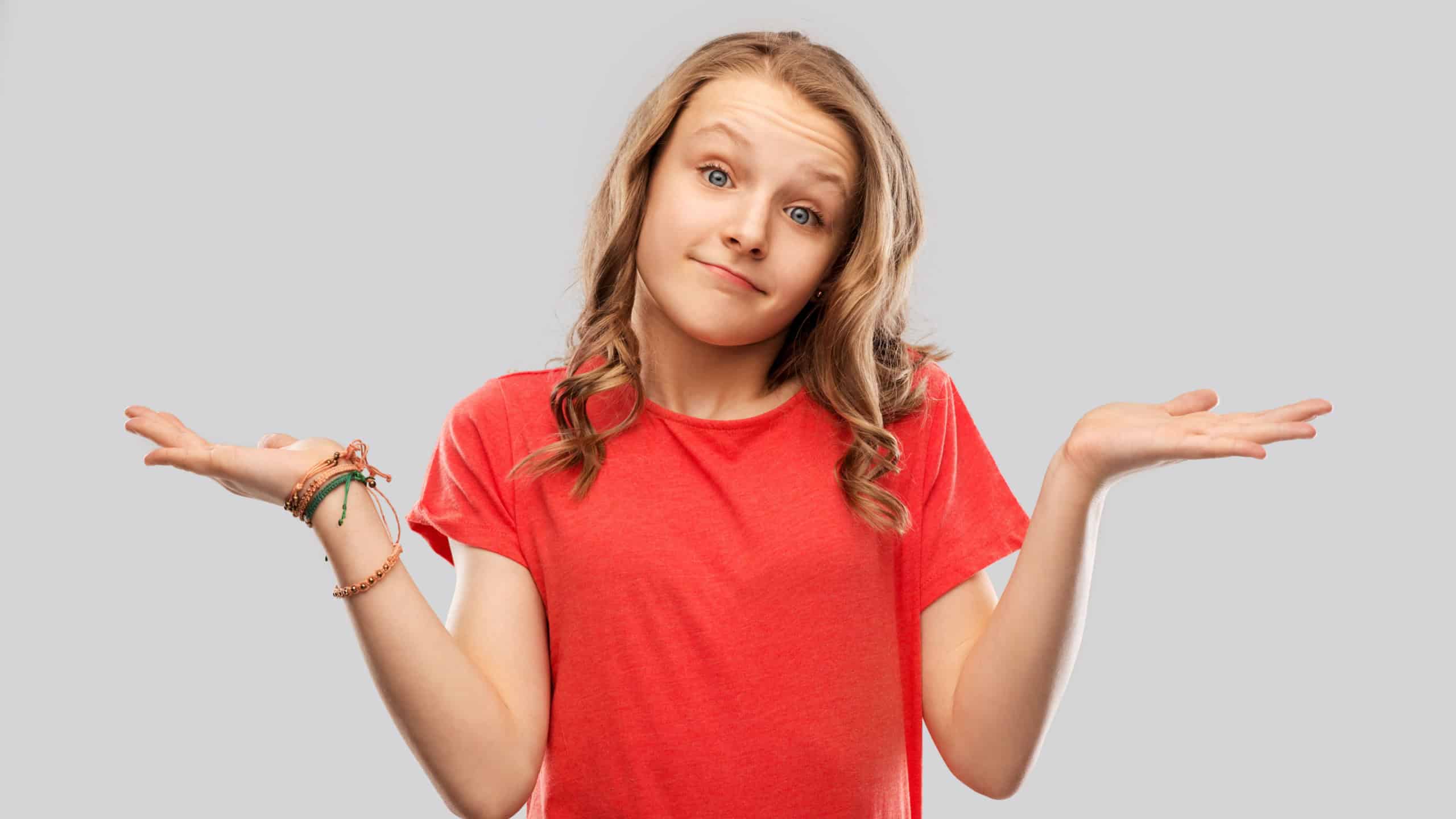 people, emotion and expression concept - wondering teenage girl in red t-shirt shrugging over grey background
