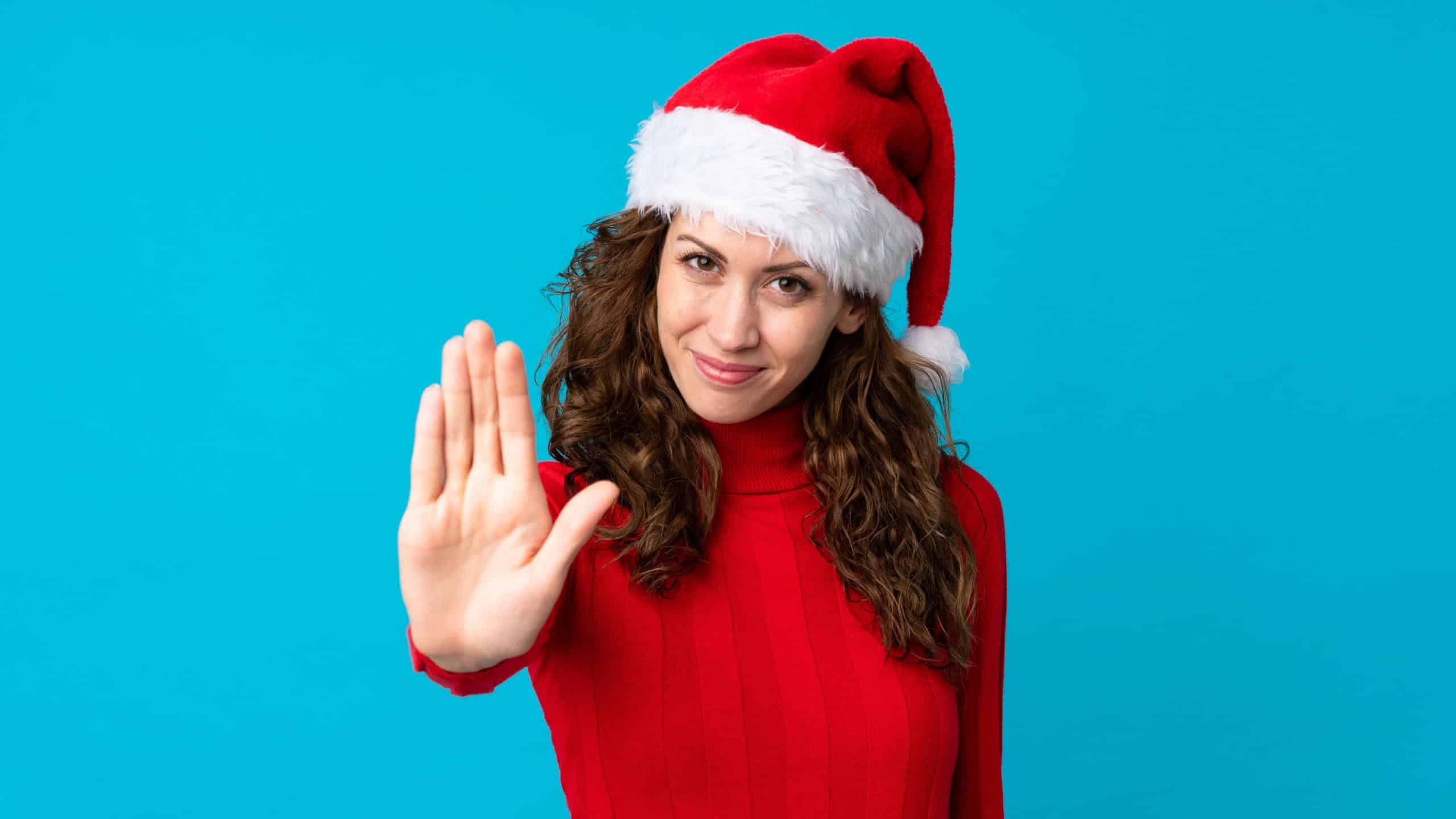 Girl with christmas hat over isolated yellow background making stop gesture with her hand