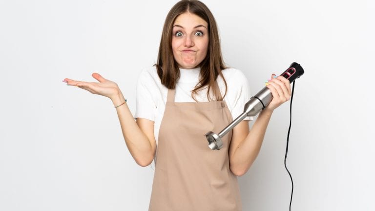 Young woman using hand blender isolated on white background having doubts with confuse face expression