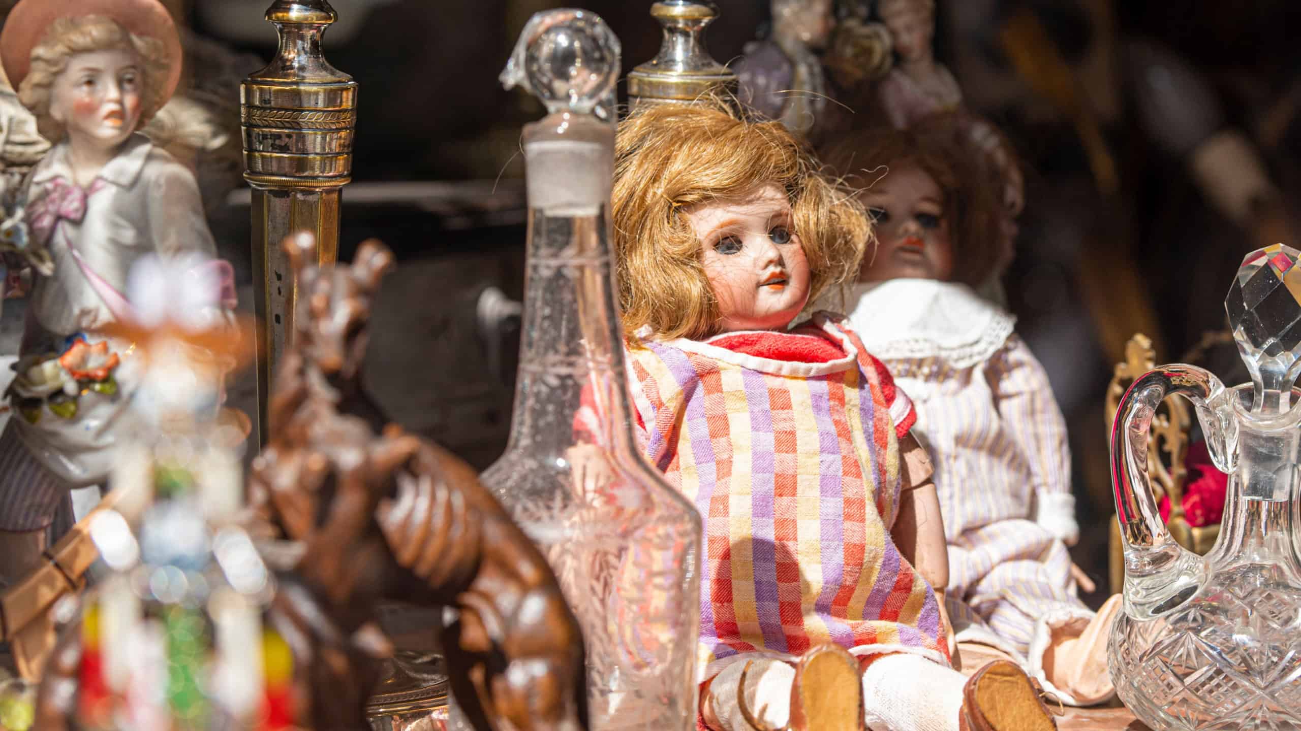 Vintage used doll at flea market with other things: porcelain figurine, glass jug, crystal decanter in France, Strasbourg
